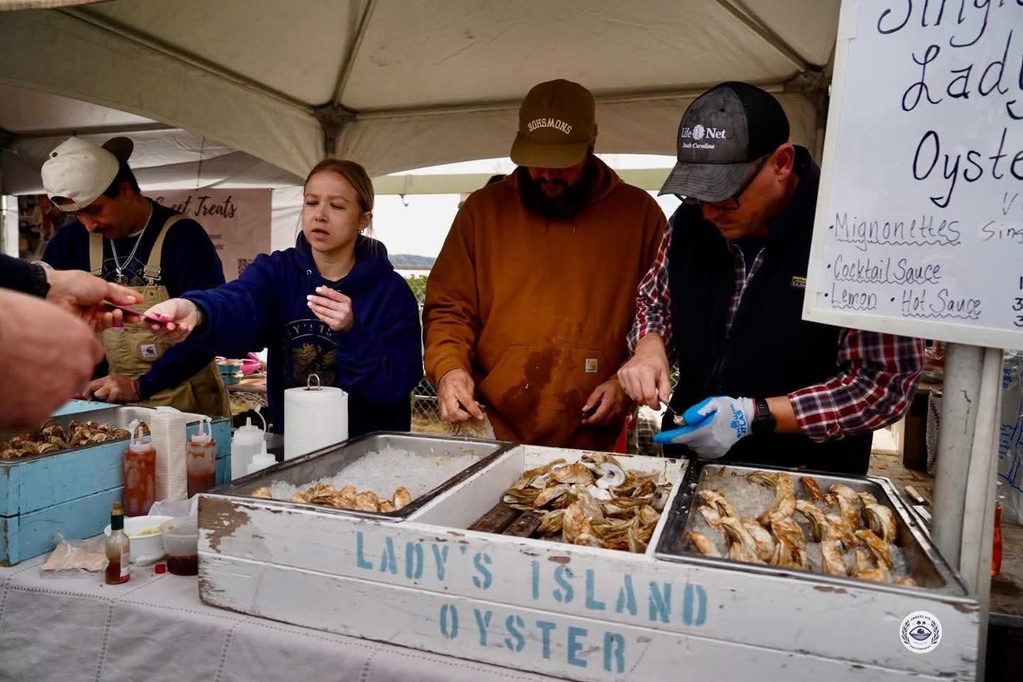 Oyster vendors serving fresh seafood at a local market, featuring a woman handing an oyster to a customer while two men prepare oysters at a booth labeled 