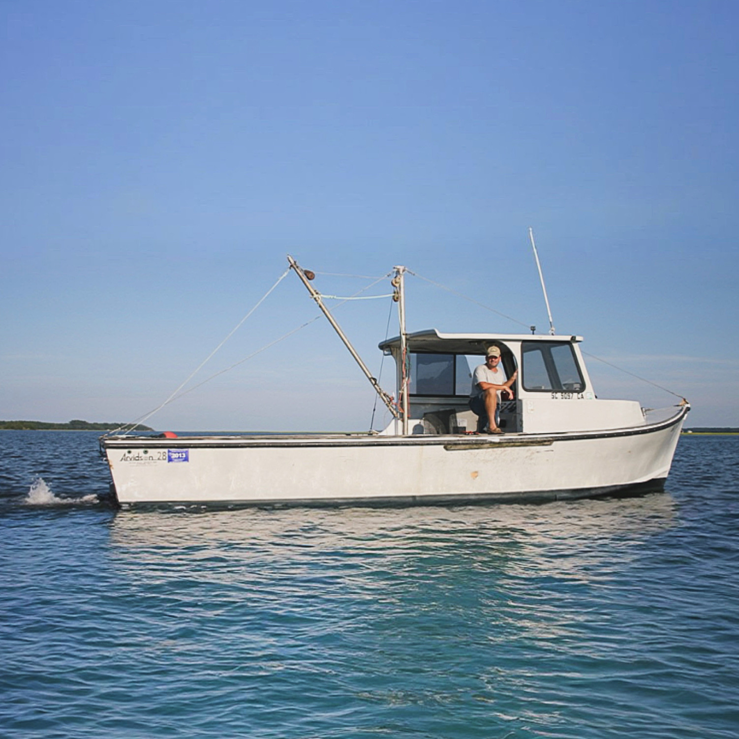 A small fishing boat cruising on calm waters, with a person sitting at the helm, under a clear blue sky.